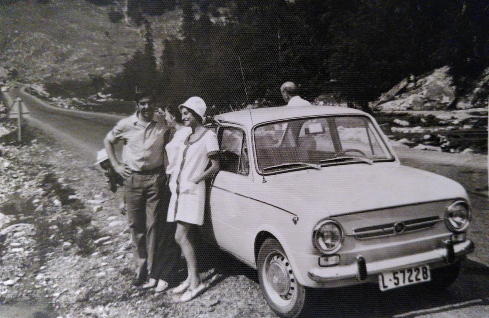 Fotografía antigua de una pareja junto a un coche clásico en un paisaje de montaña.