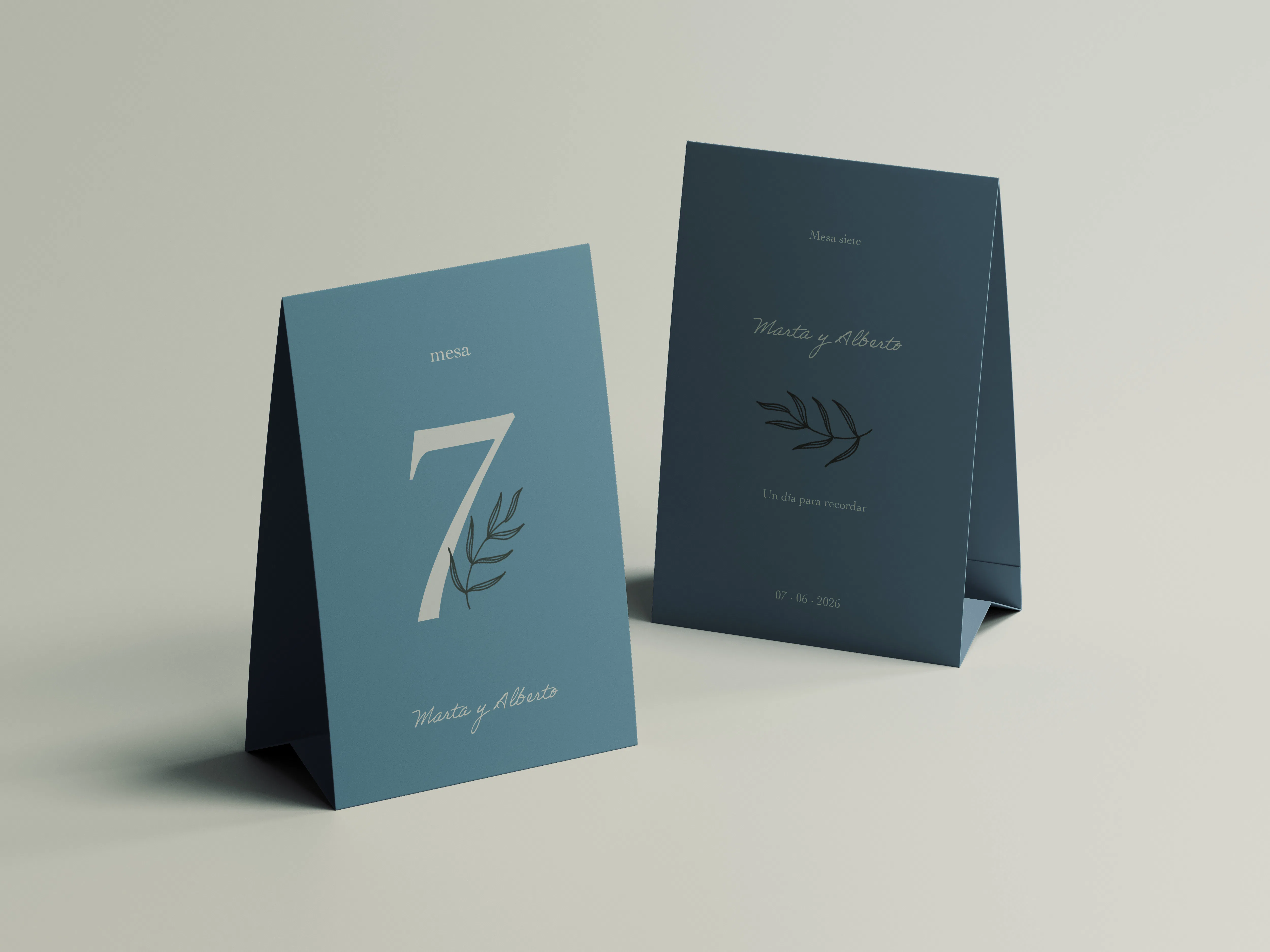 Dos minutas de boda en formato tent card, en tonos azul claro y azul marino, con nombres de mesa e ilustraciones botánicas.